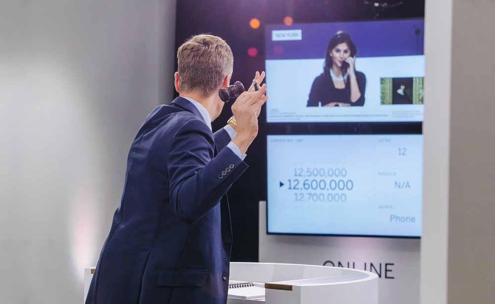 An auctioneer takes a live phone bid during Sotheby&rsquo;s hybrid online marquee sales, the screen showing a New York bidder at 12,600,000.