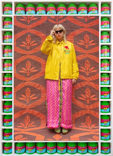 Hassan Hajjaj, portrait in a yellow jacket against an orange textile ground, framed with rows of tins